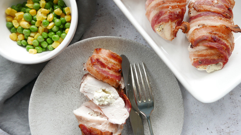 Stuffed chicken breasts placed on two different plates and a small bowl of peas with corn kernels.