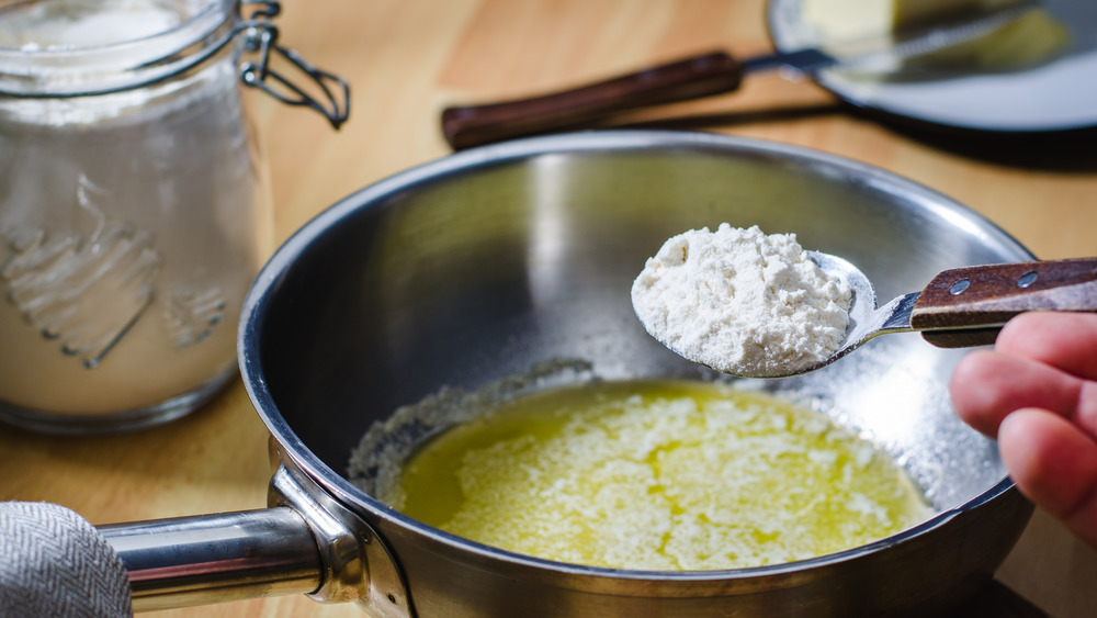 Hand holding spoon with cornstarch over metal pot