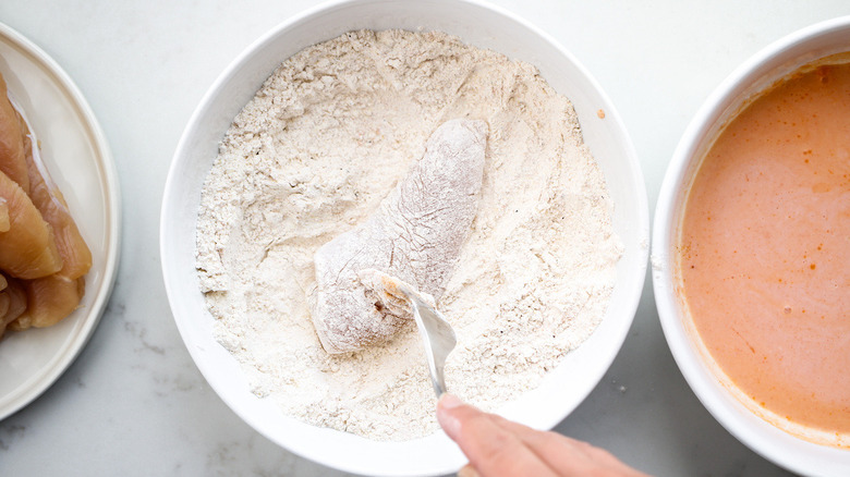 hand coating chicken with flour