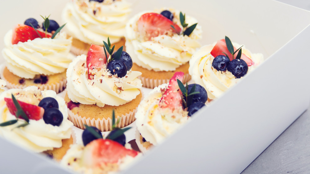 cupcakes in a box topped with fruit and frosting