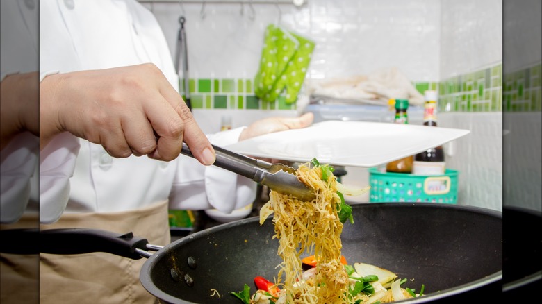 Person holding chow mein with tongs