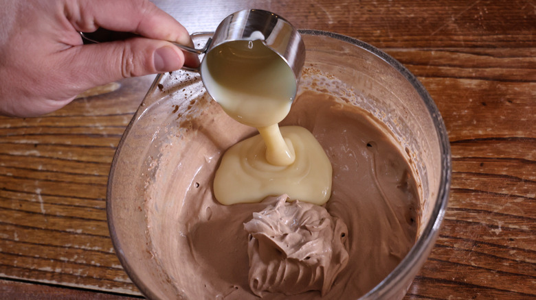 pouring condensed milk into bowl of chocolate whipped cream