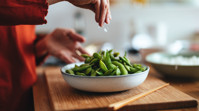 Person sprinkling salt on edamame