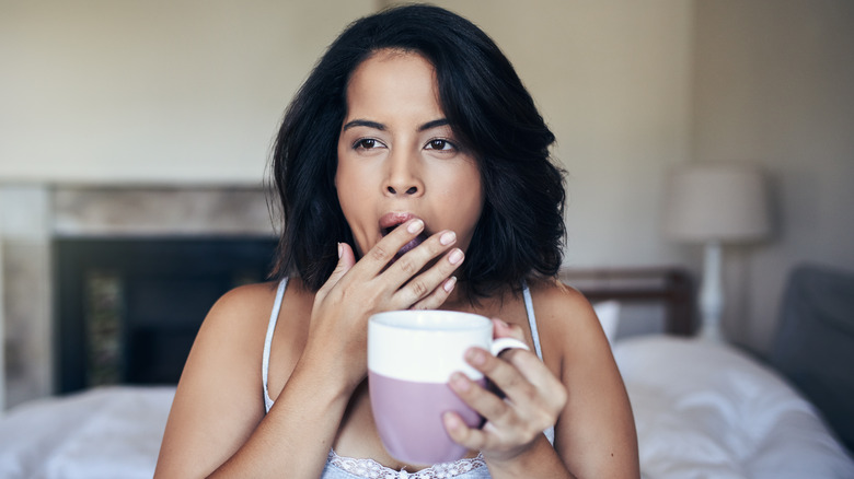 woman yawning holding coffee mug