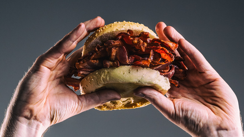 Hands holding bacon sandwich