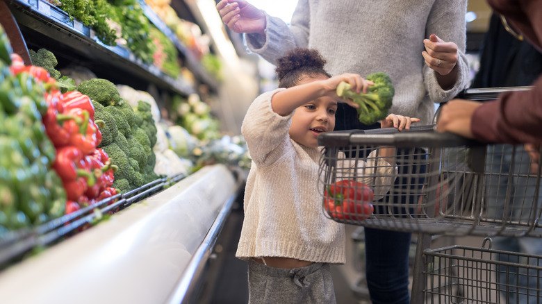 Child putting broccoli in shopping cart