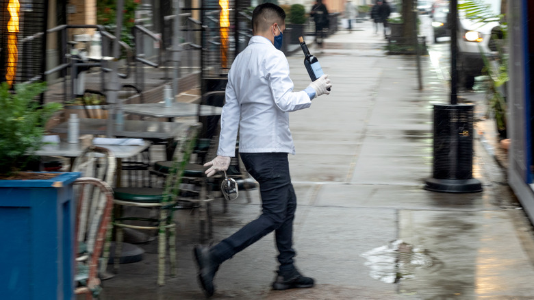 Waiter in face mask carrying wine