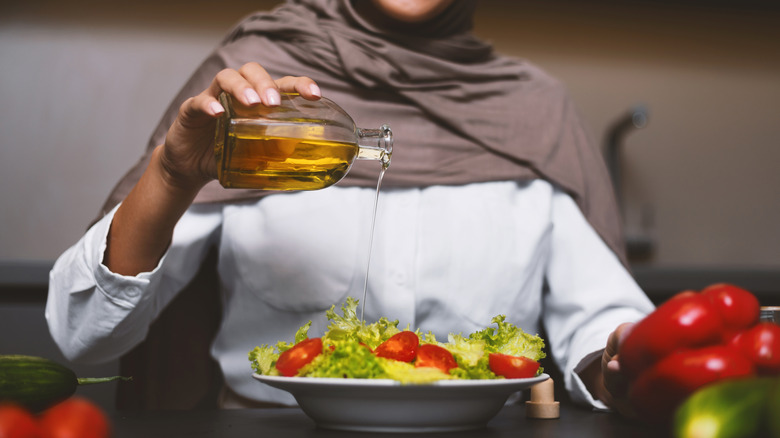 person drizzling oil over salad