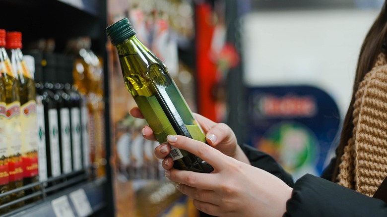 person looking at bottle of olive oil in store