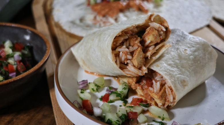 sliced butter chicken burrito on plate with kachumber.