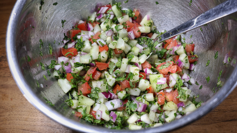 metal mixing bowl full of diced cucumber, tomato, and red onion with minced herbs