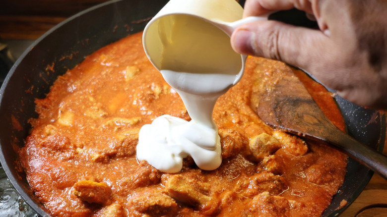 hand pouring cream into skillet of tomato-based curry