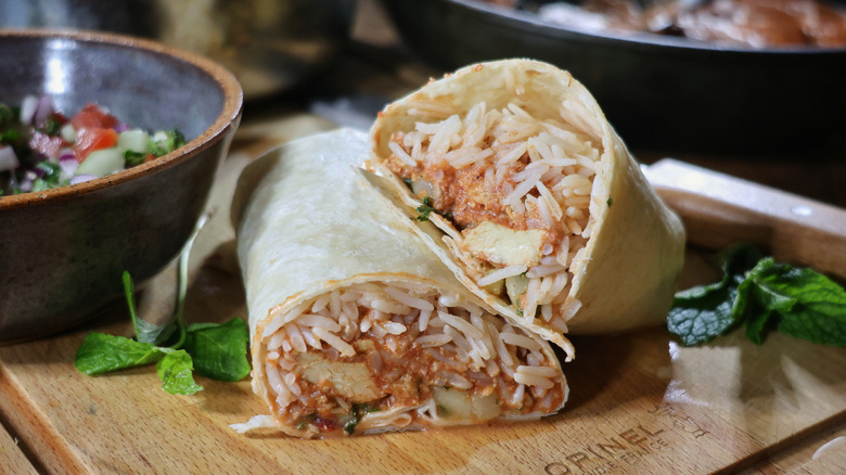 sliced butter chicken burrito on cutting board with mint leaves