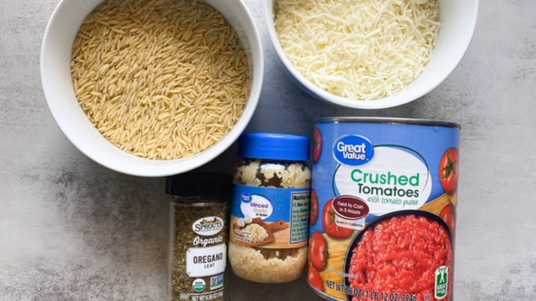 Orzo and shredded mozzarella in bowls, dried oregano, jar of minced garlic, can of crushed tomatoes