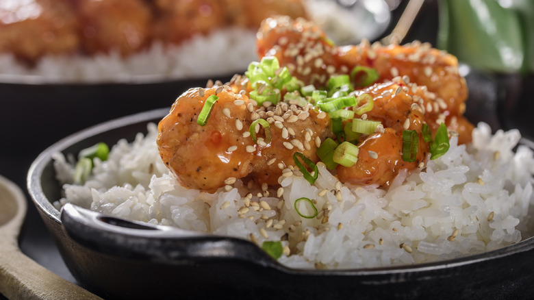 Orange chicken over white rice topped with green onions and sesame seeds