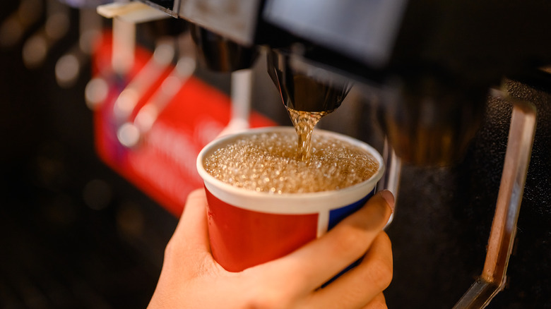 person filling soda cup at machine