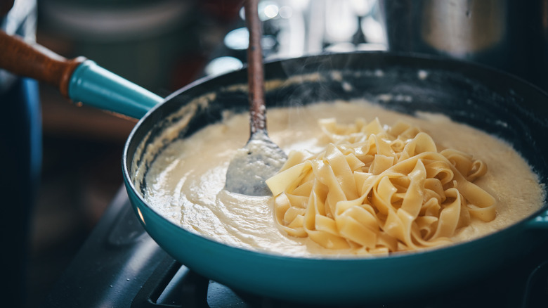 Pasta atop a pan of Alfredo sauce