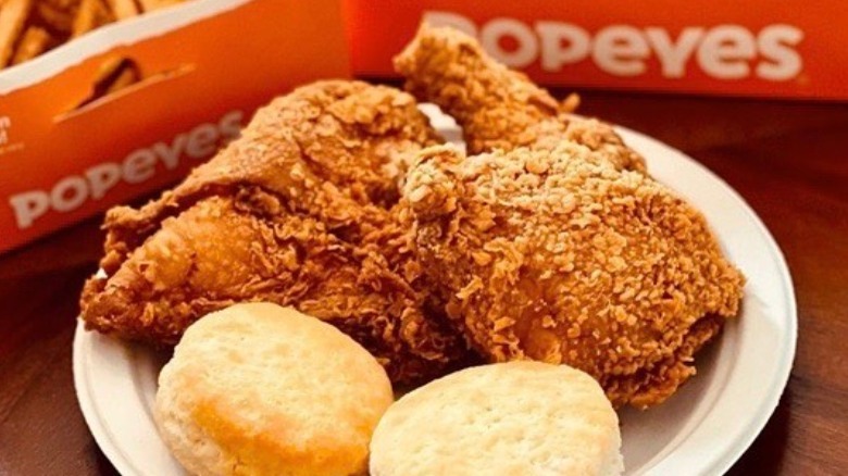 Popeyes fried chicken drumsticks and biscuits on paper plate