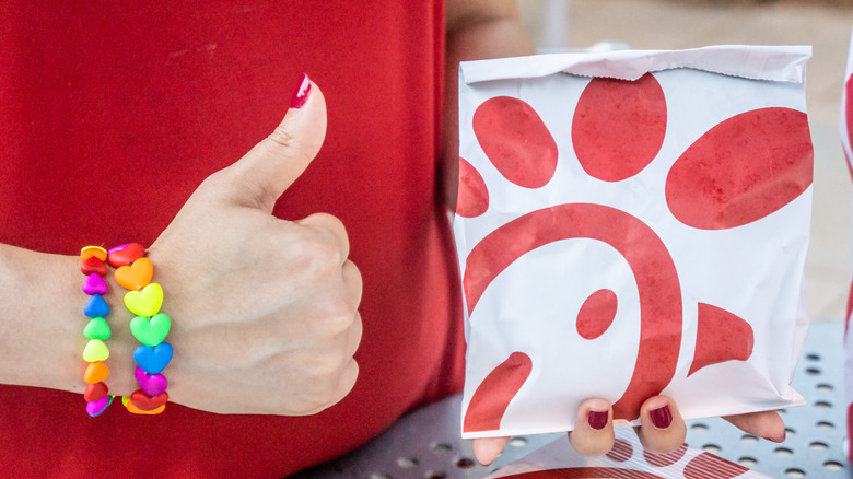 Person holding a Chick-Fil-A bag, giving thumbs-up