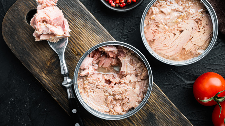 Tuna on utensil, two cans of tuna on cutting board