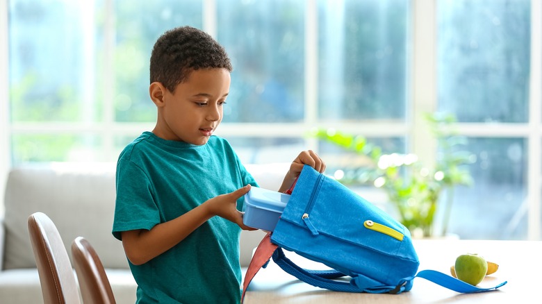 Kid putting lunch in his school backpack