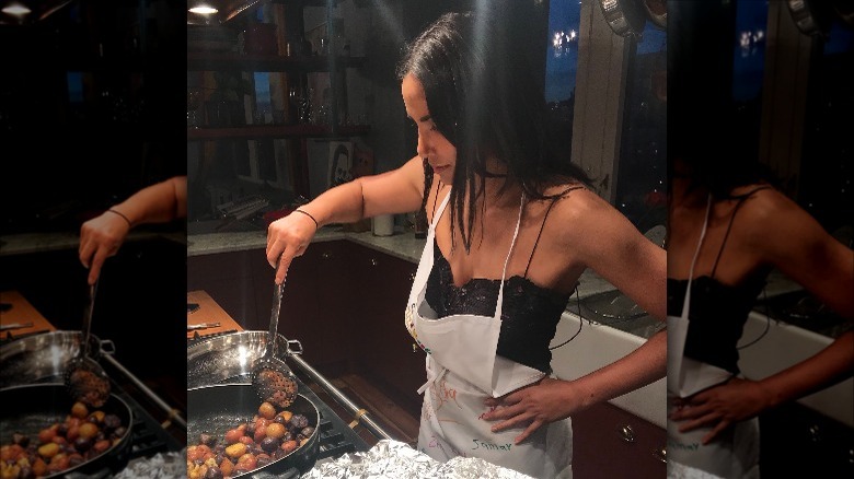 Padma Lakshmi stirring potatoes on the stove with one hand on her hip