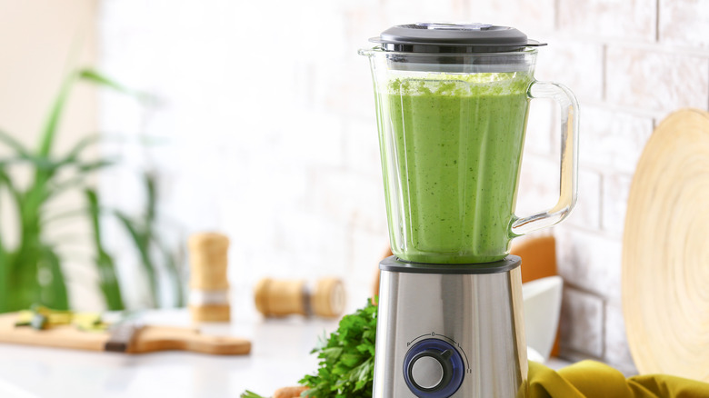 green smoothie in a blender surrounded by ingredients