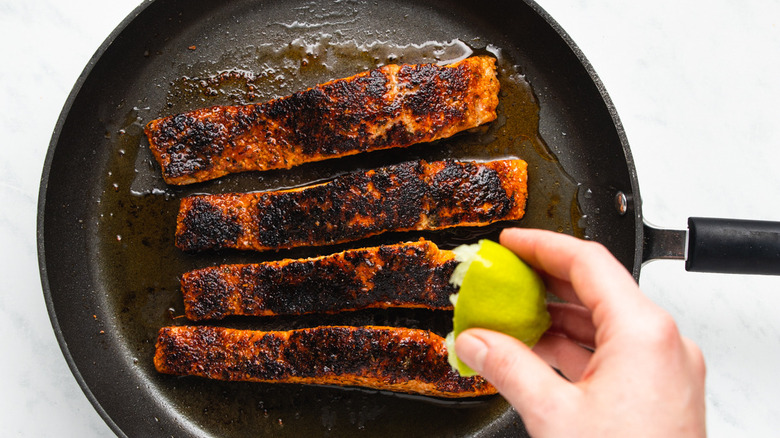 Lime being squeezed over pan-seared blackened salmon in a frying pan