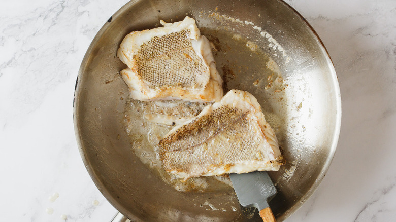 skin up grouper fillets in pan with spatula