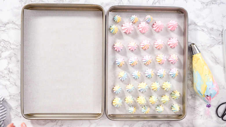 Two cookie sheets lined with parchment paper with piped icing