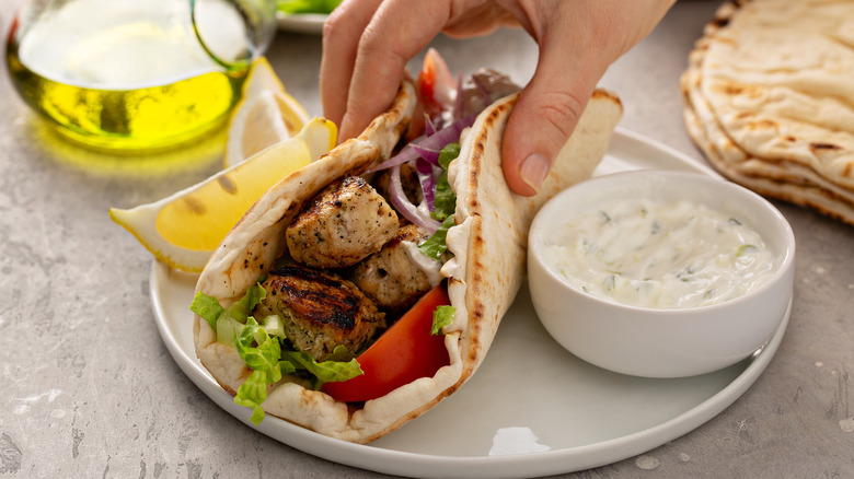 person holding pita of souvlaki with tzatziki