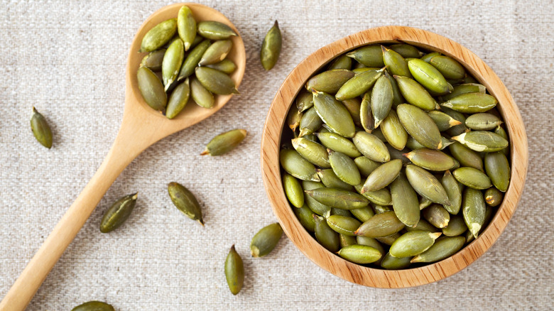 Green pepitas in wooden bowl next to spoon