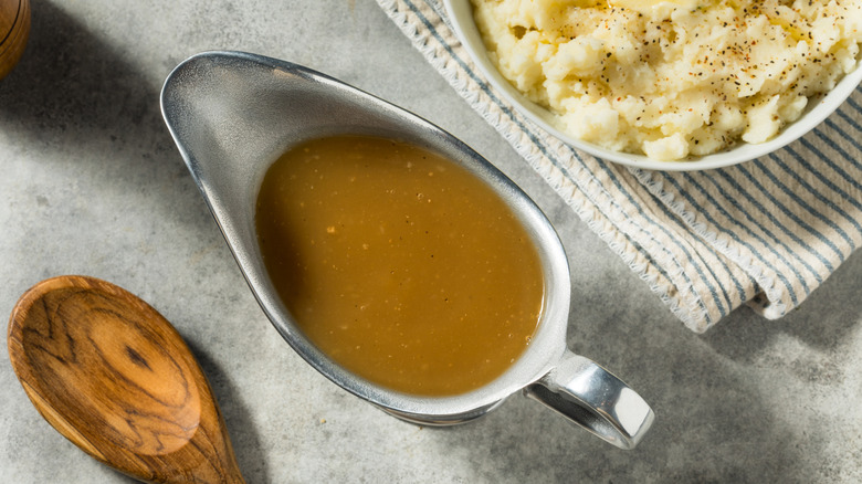 A filled gravy boat and beside a bowl of mashed potatoes and a wooden spoon