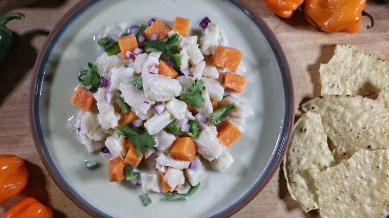 plate of Peruvian-style ceviche with leche de tigre on wooden board with corn chips and chiles surrounding it