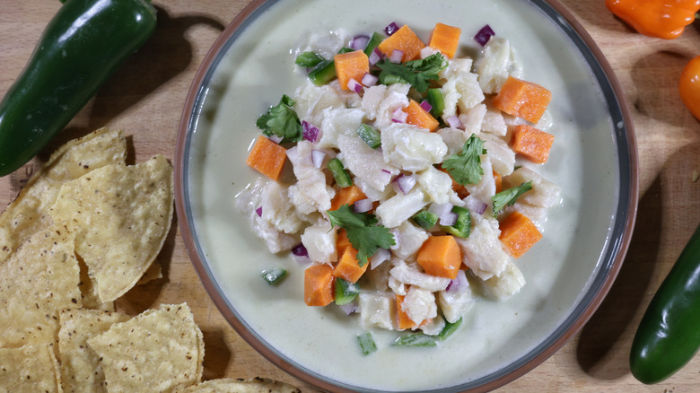 plate of ceviche with leche de tigre on cutting board surrounded by corn chips and chiles