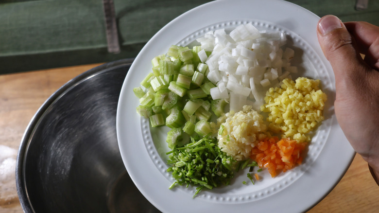 hand dumping plate of finely diced celery, onion, garlic, ginger, habanero, and cilantro stems into mixing bowl