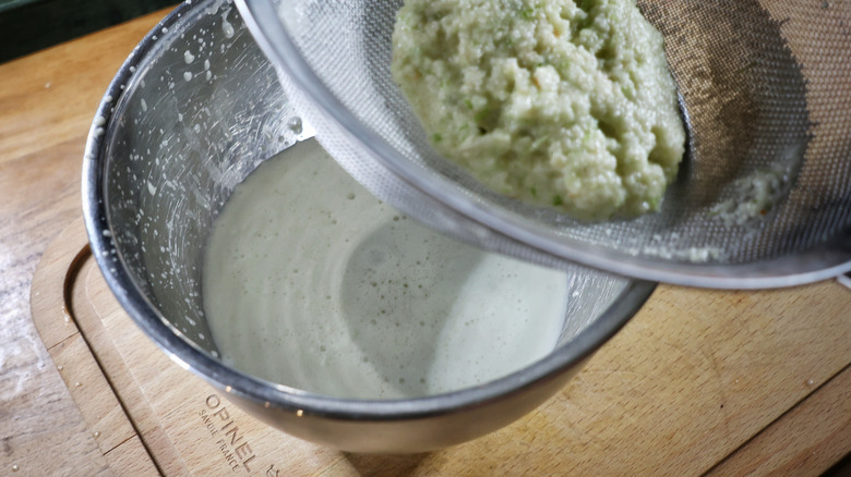 bowl of leche de tigre with sieve of strained ingredients above it