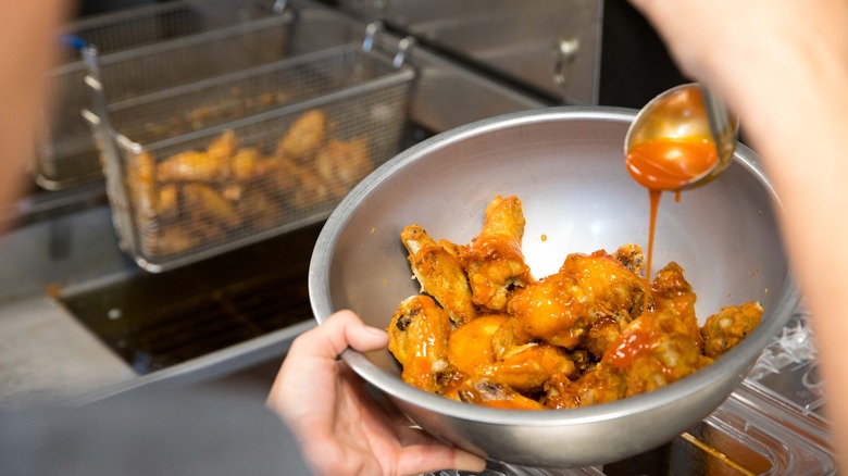 pouring sauce on chicken wings 