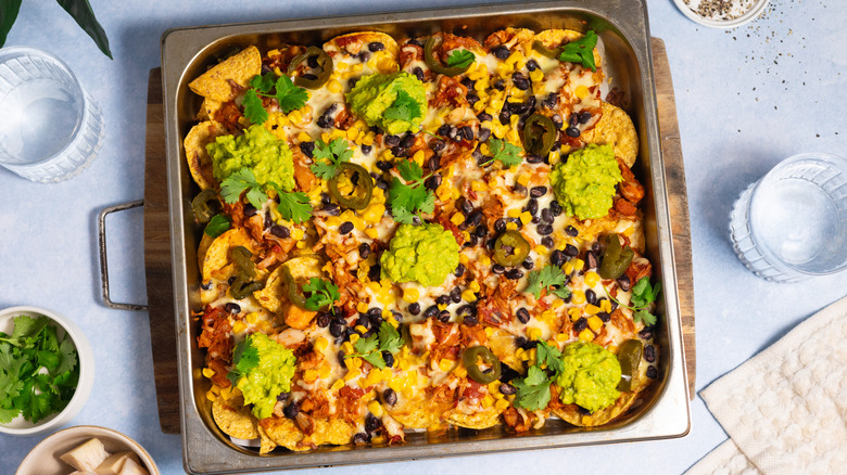 vegan cheese nachos with jackfruit, guacamole, beans, and corn on baking tray