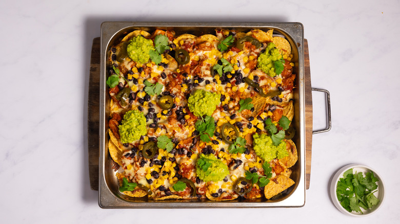 nachos in baking tray with corn, black beans and guacamole