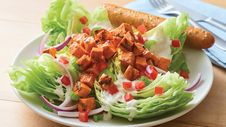 white plate featuring buffalo chicken wedge salad with a breadstick and glass of beer