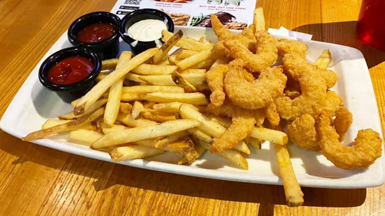 white plate of double crunch shrimp with a side of seasoned fries and dipping sauces on a wooden table at Applebee's