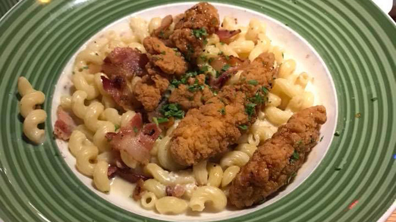 green plate of four cheese mac and cheese with honey pepper chicken and a bread stick on the side