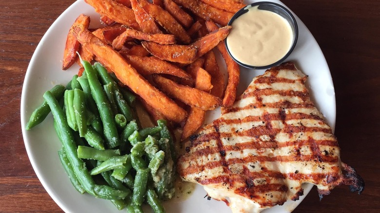 grilled chicken breast on a white plate served with sweet potato fries and garlicky green beans