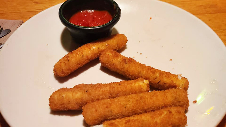 crispy mozzarella sticks on a white plate with marina sauce for dipping