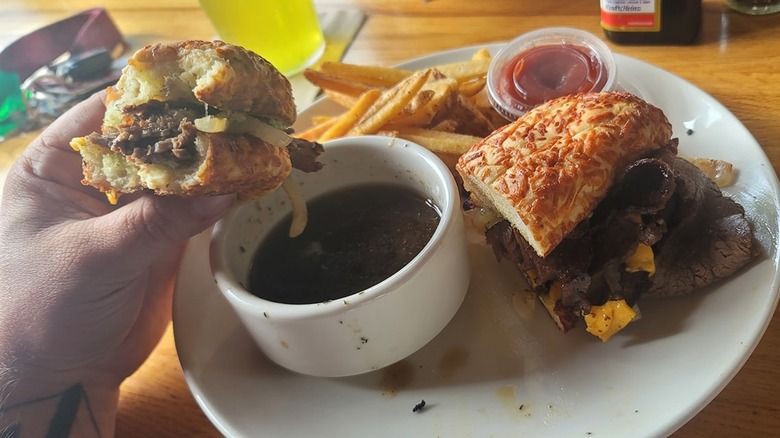 Applebee's prime rib dipper sandwich on a white plate with seasoned fries and a white ceramic bowl of au jus