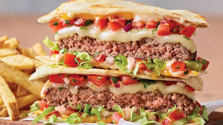 quesadilla burger with seasoned fries on a wooden board on a wooden counter