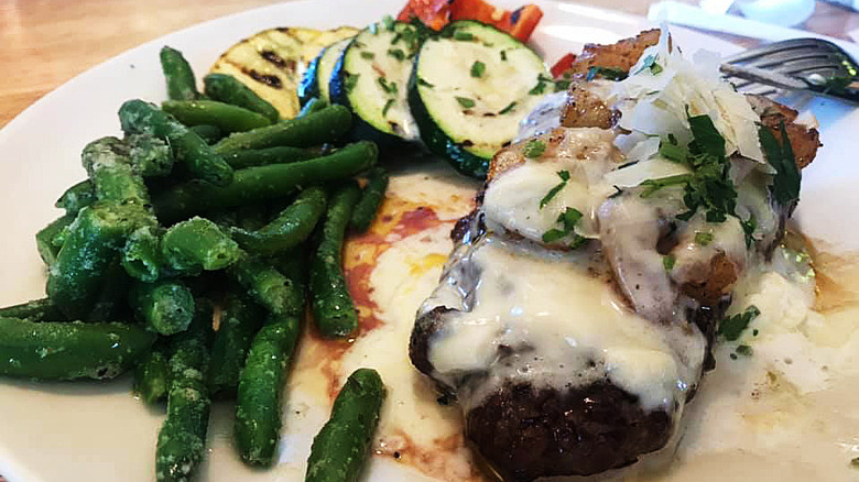 sirloin smothered with cheese, shrimp, and onions alongside garlicky green beans and fresh roasted vegetables on a white plate