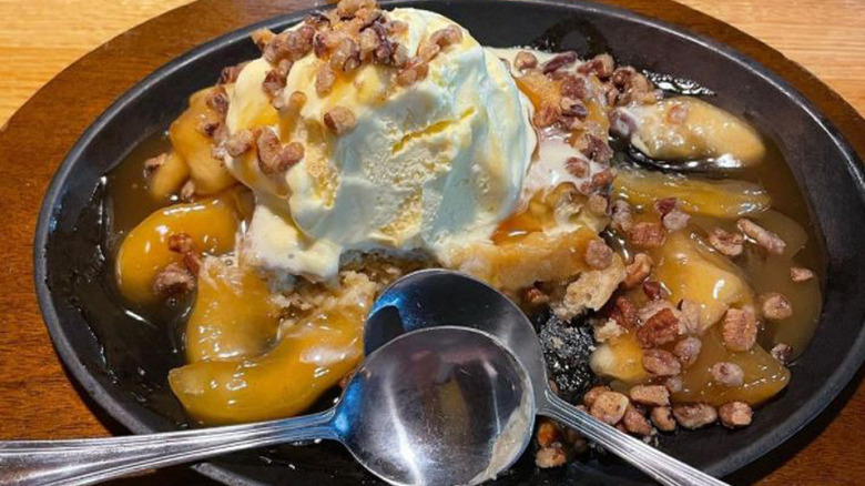 sizzlin' caramel apple blondie made with vanilla ice cream, candied pecans, buttery cinnamon apple slices, and a butter pecan blondie on a black plate with two spoons