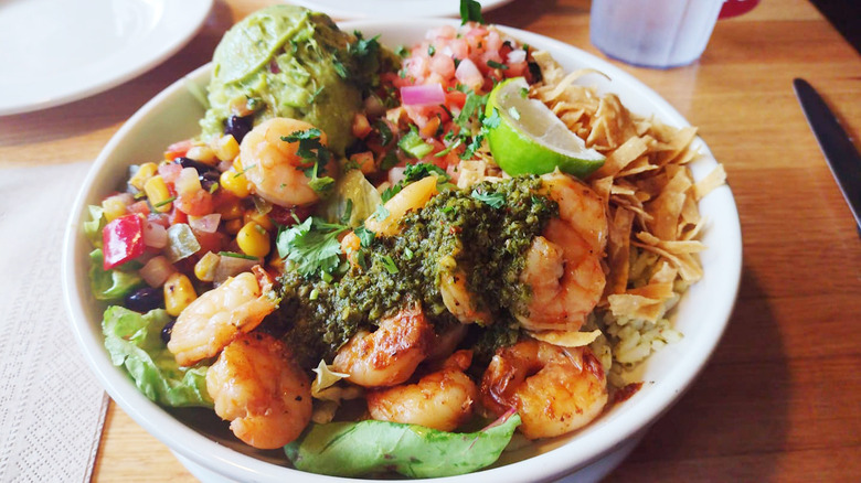 white bowl of Tex Mex shrimp bowl on a wooden table near a glass of water and a knife